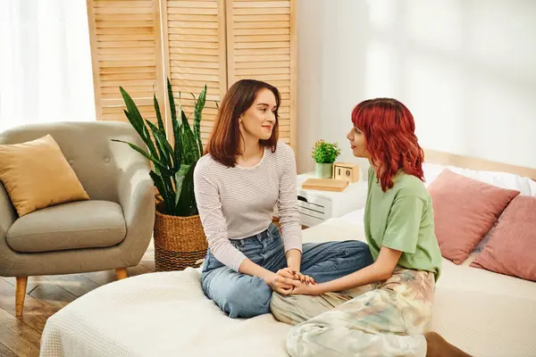 Young lgbt couple in casual attire sharing cozy moment and sitting together in sunny bedroom - foto de stock
