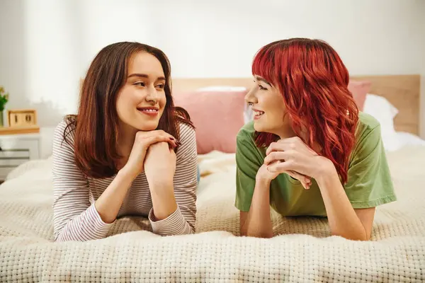 Cheerful young lgbt couple in casual attire having cozy moment and looking at each other on bed — Stock Photo