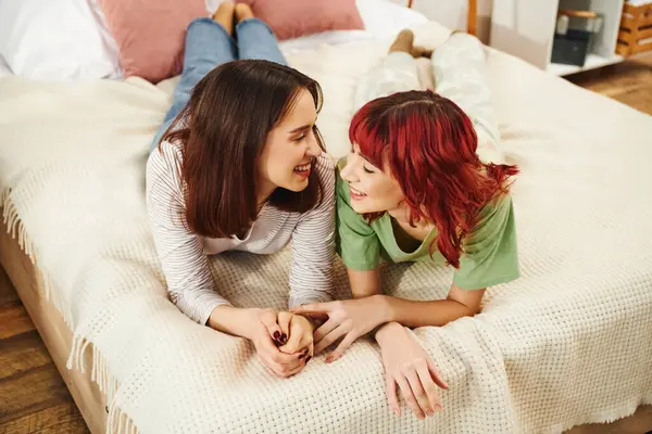 Overhead view of happy lesbian couple smiling at each other while having cozy moment on bed - foto de stock