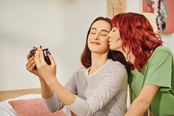 Candid home photo session of happy young lesbian couple taking selfie on retro camera, kiss — Stock Photo