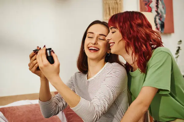 Candid home photo session of excited young lesbian couple taking selfie on retro camera in bedroom — Stock Photo