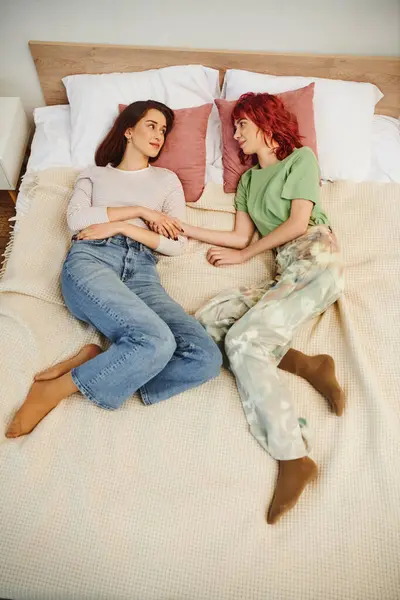 Щаслива молода лесбіянка пара тримає руки, лежачи разом на ліжку, дивлячись один на одного — стокове фото