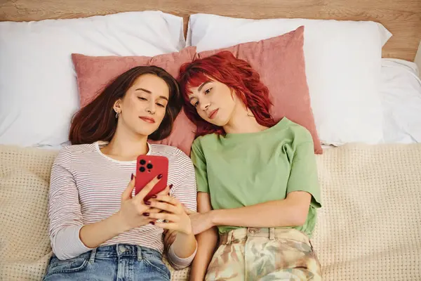 Vista superior de la joven pareja lesbiana tomando selfie en el teléfono inteligente mientras está acostado en la cama, foto de las redes sociales - foto de stock