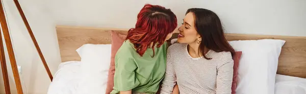 Horizontal banner of happy young lesbian couple in casual wear going to kiss while sitting on bed — Stock Photo