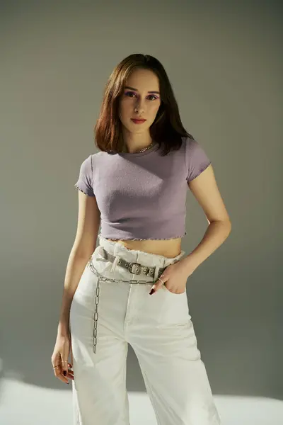 Stylish gen z woman in 20s posing in purple t-shirt, standing with hand in pocket of white jeans — Stock Photo