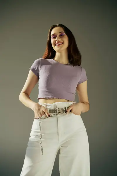 Sorridente gen z donna negli anni '20 in posa in t-shirt viola, in piedi con le mani in tasche di jeans bianchi — Foto stock