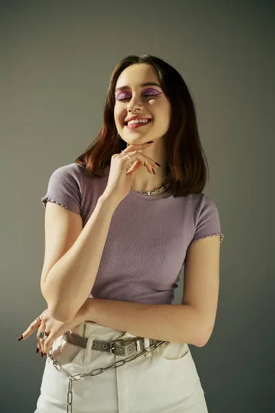 Bold makeup of happy gen z girl in 20s posing in purple t-shirt and white jeans, with closed eyes - foto de stock