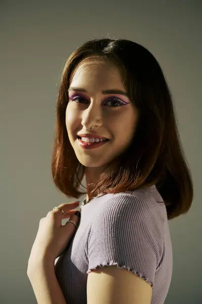 Bold makeup of pleased gen z girl posing in t-shirt and looking at camera, purple eye shadow — Stock Photo