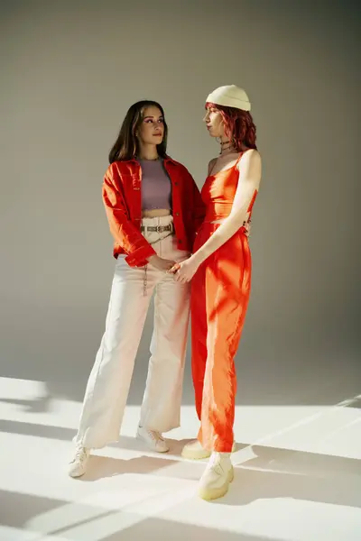 Elegante giovane coppia lesbica in abiti vivaci che si tiene per mano su sfondo grigio, condividendo il momento tenero — Foto stock
