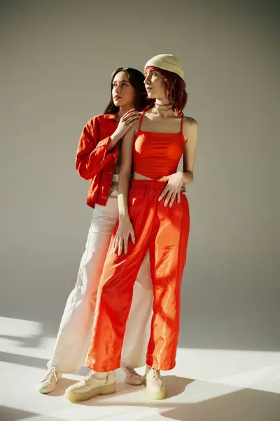 Полная длина стильных женщин в яркой одежде, стоящих вместе на сером фоне, лесбийская пара — стоковое фото