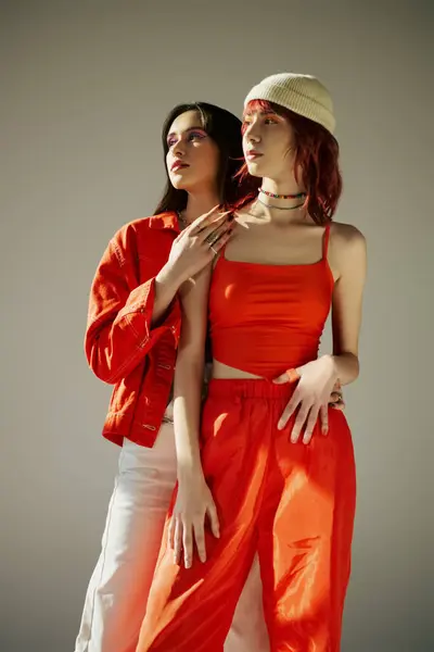 Zwei stilvolle Frauen in lebendiger Kleidung, die zusammen vor grauem Hintergrund stehen, ein modisches lesbisches Paar — Stockfoto