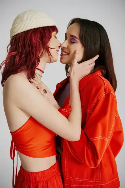 Heureux élégant couple lesbien avec audacieux maquillage en tenue vibrante baisers sur fond gris — Photo de stock