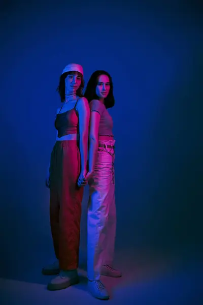 Щасливі подружки 20-х років, з сміливим макіяжем і стильним вбранням, тримаючи руки під фіолетовими вогнями — стокове фото