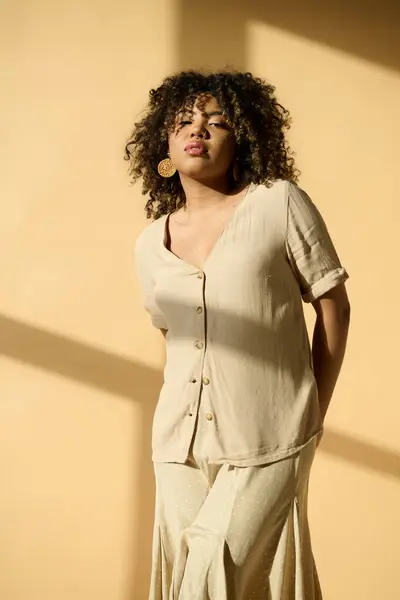 A beautiful young African American woman with curly hair standing gracefully in front of a vibrant yellow wall. — Stock Photo