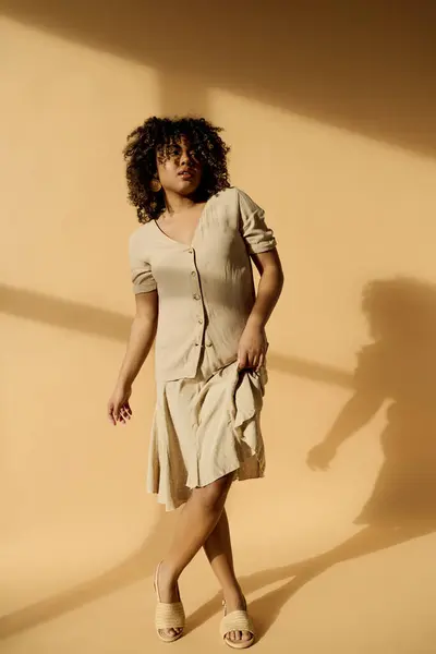 A beautiful young African American woman with curly hair stands in a room, casting a striking shadow on the wall. — Stock Photo
