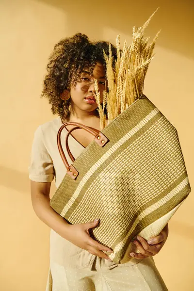 Красивая молодая афроамериканка с вьющимися волосами держит в руках корзину пшеницы, олицетворяющую изобилие и урожай.. — стоковое фото
