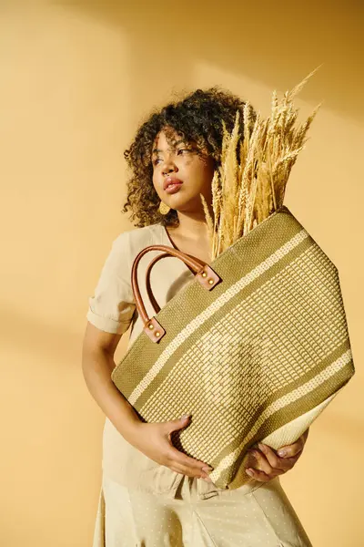 A beautiful young African American woman with curly hair holds a basket brimming with wheat stalks, exuding a serene presence. — Stock Photo