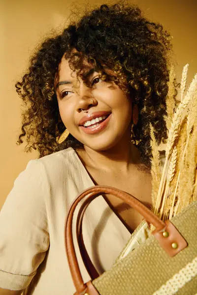 A beautiful young African American woman with curly hair smiling while holding a brown purse in a studio setting. — Stock Photo