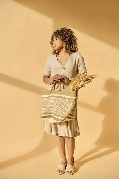 A beautiful young African American woman with curly hair holding a basket filled with golden wheat in a peaceful studio setting. — Stock Photo