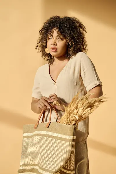 Stylish young African American woman holding a shopping bag and sheaf of wheat in a studio setting. — Stock Photo