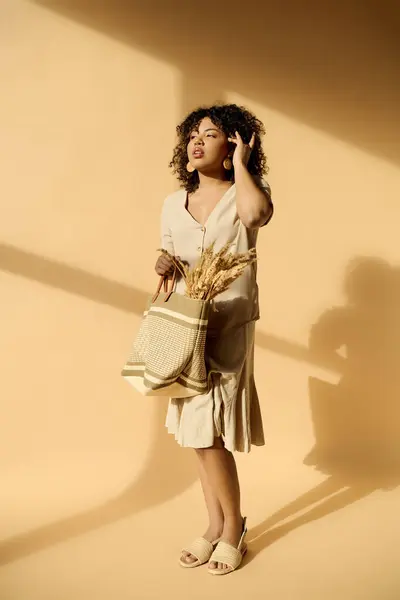 Uma mulher afro-americana elegante com cabelo encaracolado fica segurando um saco em um vestido de verão elegante. — Fotografia de Stock