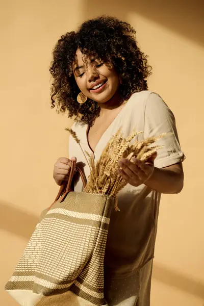 A beautiful young African American woman with curly hair holds a bag filled with wheat, embodying a connection to nature and abundance. — Stock Photo
