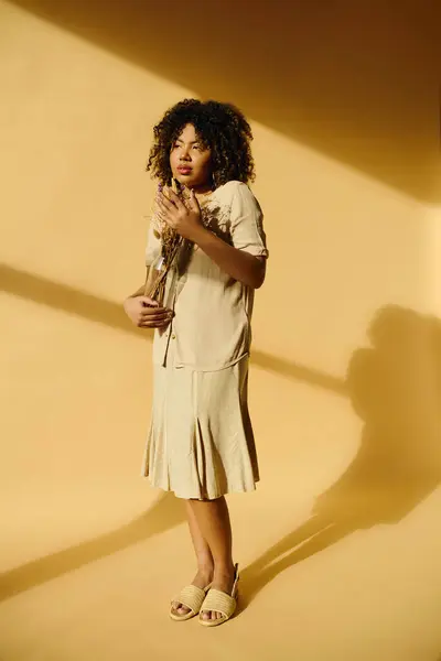 Une belle jeune femme afro-américaine aux cheveux bouclés se tient en confiance devant un mur jaune vibrant. — Photo de stock