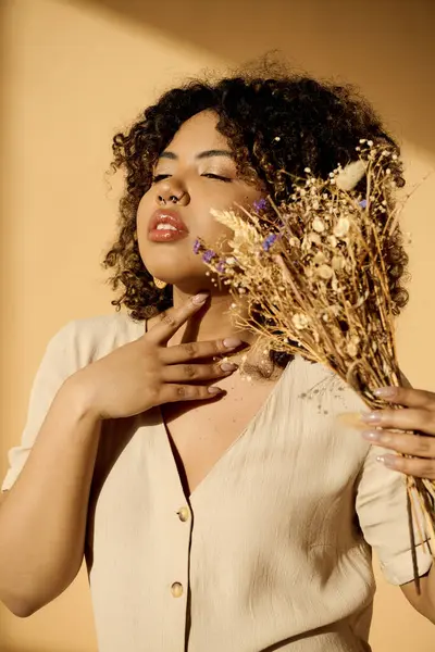 A beautiful young African American woman with curly hair holding a bunch of dried flowers in a studio setting. — Stock Photo