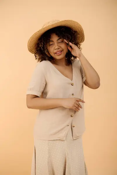 Une belle jeune afro-américaine aux cheveux bouclés, coiffée d'un chapeau et d'une robe, exsudant élégance dans un décor de studio. — Photo de stock