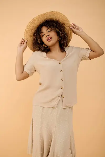 Una splendida giovane donna afroamericana, con i capelli ricci, posa elegantemente in un abito estivo ed elegante cappello in un ambiente da studio. — Foto stock