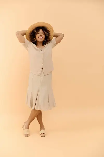 A stylish African American woman with curly hair is confidently posing in a summer dress and hat in a studio setting. — Stock Photo