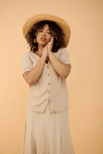 Una hermosa joven afroamericana con el pelo rizado con un vestido de verano y sombrero en un entorno de estudio. - foto de stock