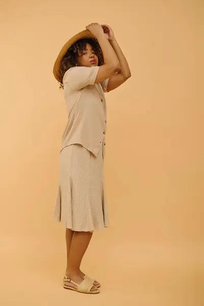Una bella giovane donna afroamericana con i capelli ricci posa con grazia in un abito estivo e cappello in un ambiente di studio. — Foto stock