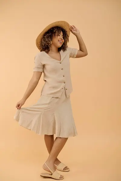 Une superbe Afro-Américaine aux cheveux bouclés, en robe d'été et chapeau, posant pour une séance photo dans un studio. — Photo de stock