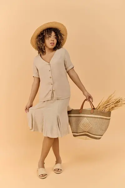 A young African American woman in a summer dress and hat, gracefully holding a basket in a studio setting. — Stock Photo