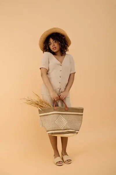 A beautiful young African American woman with curly hair holding a basket and a straw hat in a studio setting. — Stock Photo