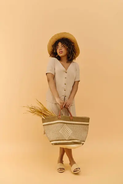 Eine schöne junge Afroamerikanerin mit lockigem Haar hält elegant einen Korb in der Hand, geschmückt mit Strohhut und Sommerkleid. — Stockfoto