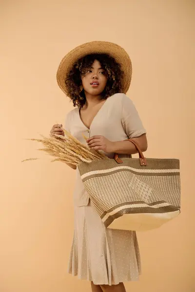A young African American woman with curly hair and a summer dress, holding a bag and wearing a straw hat. — Stock Photo