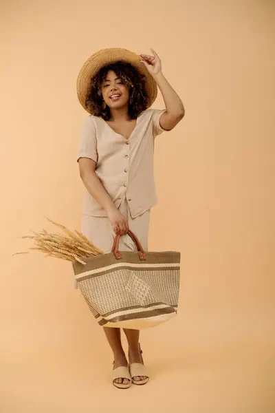 Eine schöne junge Afroamerikanerin mit lockigem Haar, trägt Hut und Kleid und hält in einem Studio einen Korb.. — Stockfoto