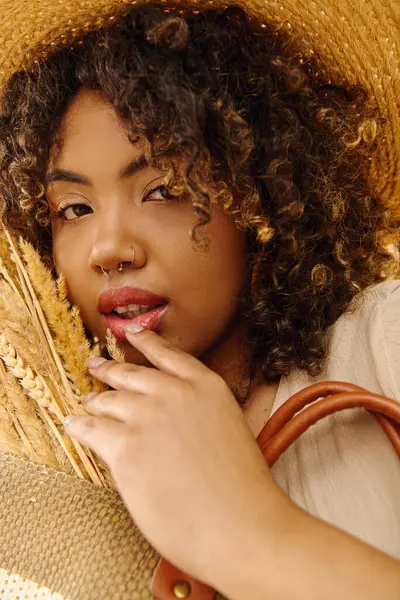 Eine stylische Afroamerikanerin mit Strohhut hält eine braune Tasche in der Hand und verströmt sommerliche Stimmung in einem Studio-Ambiente. — Stockfoto