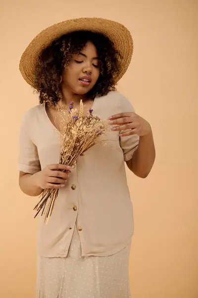 Стильная афроамериканка в шляпе грациозно держит букет ярких цветов в студии. — стоковое фото