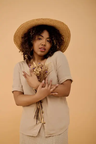 A stunning young African American woman with curly hair, wearing a straw hat, holding a vibrant bouquet of flowers. — Stock Photo