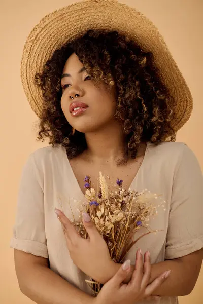 A graceful African American woman, with curly hair, wearing a straw hat, holding a vibrant bouquet of flowers. — Stock Photo