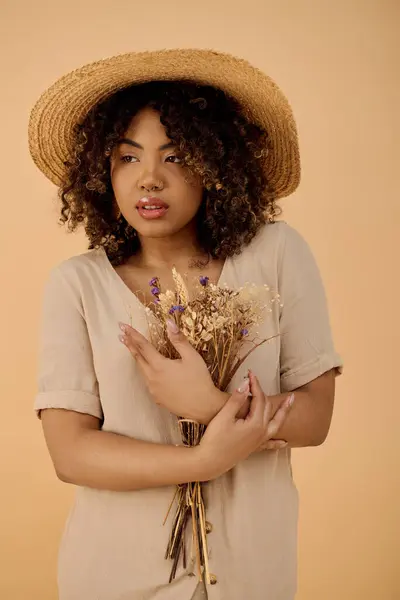 Jeune femme afro-américaine aux cheveux bouclés et robe d'été tenant un bouquet de fleurs, exsudant beauté et grâce. — Photo de stock