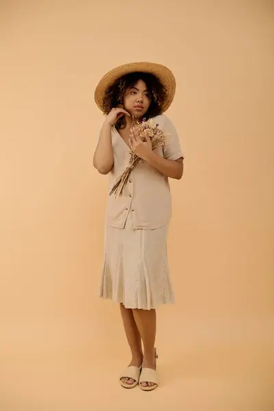 Eine stylische junge Afroamerikanerin mit lockigem Haar posiert selbstbewusst in Sommerkleid und Hut für ein Porträt. — Stockfoto