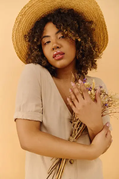 Eine schöne junge Afroamerikanerin mit lockigem Haar trägt einen Strohhut und hält einen Strauß bunter Blumen in der Hand. — Stockfoto