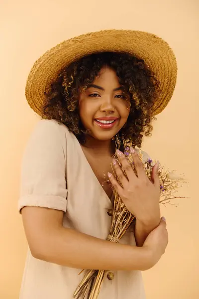 Молода афроамериканка, в солом'яному капелюсі, тримає купу квітів в студійній обстановці. — стокове фото
