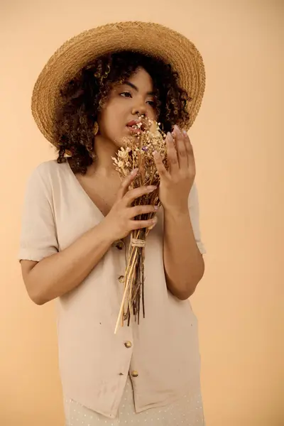 A young African American woman with curly hair wearing a straw hat, holding a vibrant bunch of flowers in a studio setting. — Stock Photo