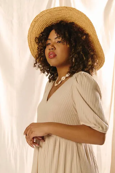 Uma jovem afro-americana com cabelo encaracolado posa elegantemente em um vestido de verão e um chapéu de palha elegante. — Fotografia de Stock