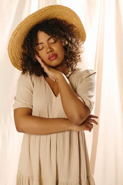A young African American woman with curly hair wearing a straw hat and a summer dress exudes ethereal beauty in a studio setting. — Stock Photo